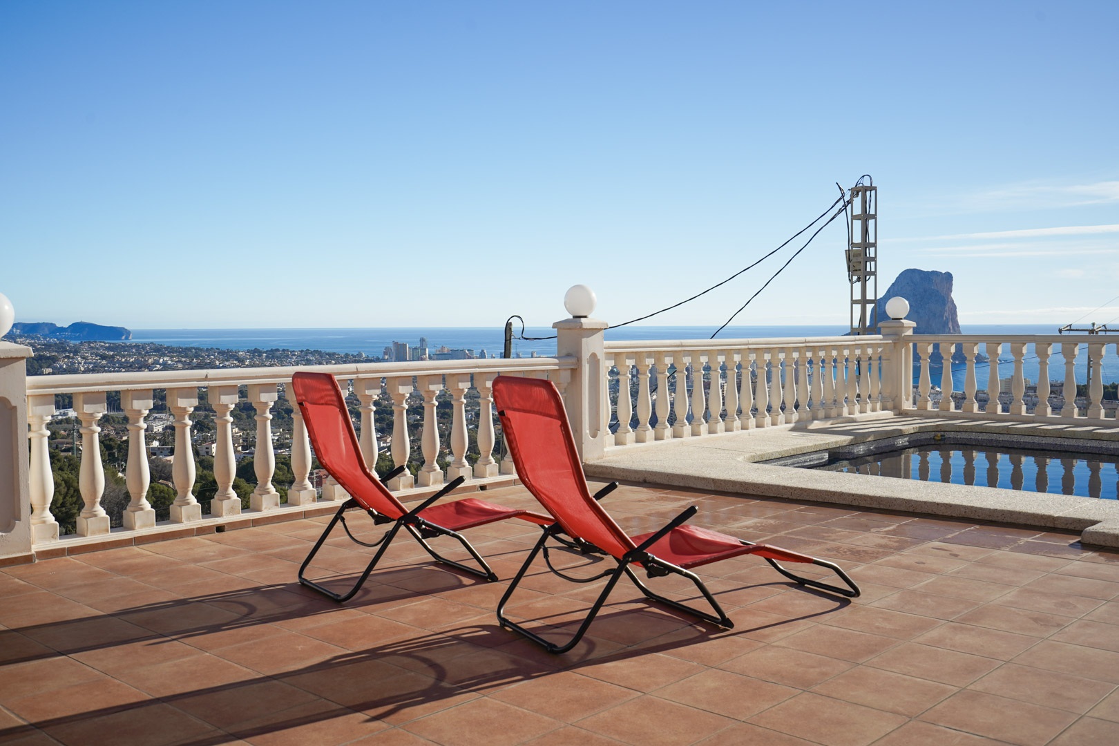 Terraza elevada con suelo de baldosas de terracota, balaustrada blanca y vistas panorámicas al Peñón de Ifach y al mar Mediterráneo junto a la piscina.