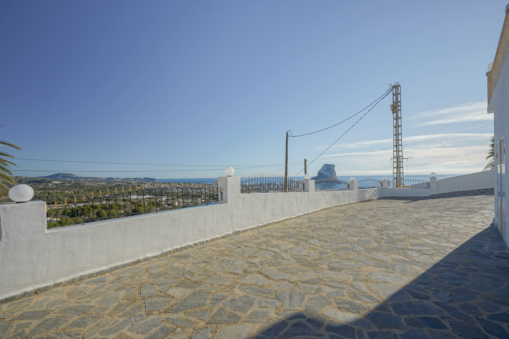 Terraza pavimentada con piedra natural que ofrece vistas panorámicas al Peñón de Ifach y la costa de Calpe, delimitada por un muro blanco con forja.