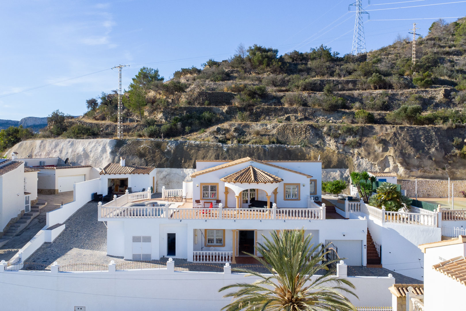 Vista exterior de la villa de dos niveles con fachada blanca, amplias terrazas con balaustradas, piscina privada y cocina de verano bajo la Sierra de Oltà.
