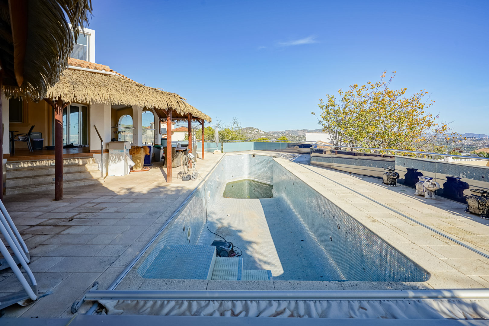 Área de piscina exterior con solárium de piedra, pérgola de estilo rústico y barandillas de cristal que ofrecen vistas despejadas a las montañas.