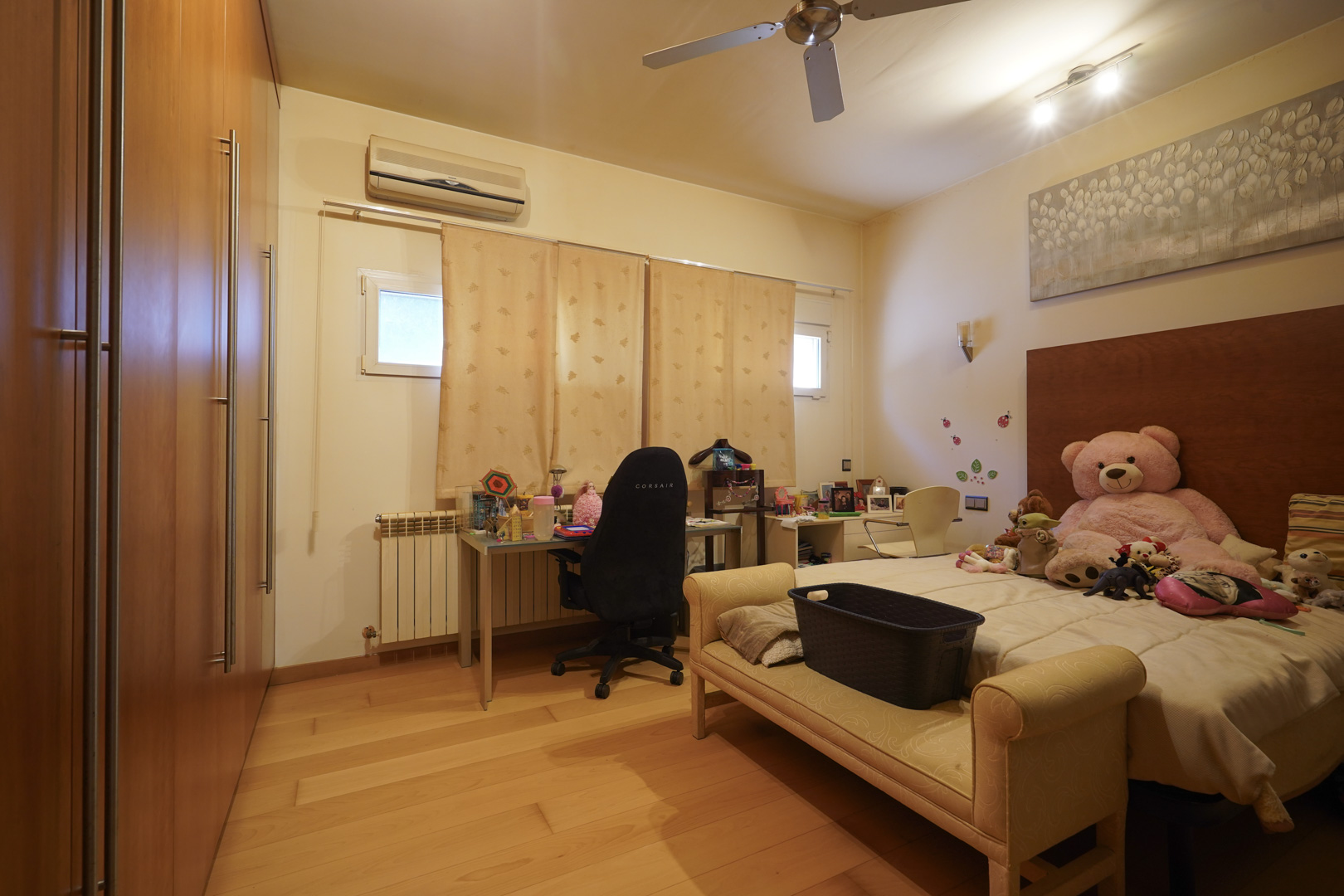 Dormitorio con suelos de madera noble, amplios armarios empotrados, zona de escritorio, aire acondicionado y ventilador de techo.