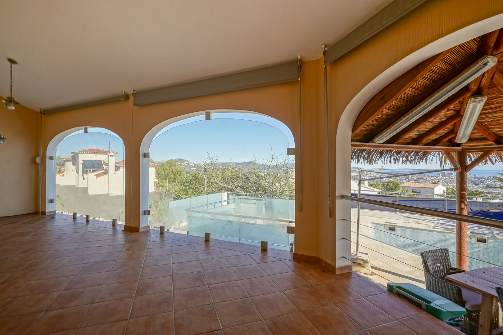 Terraza cubierta con suelos de terracota y arcos acristalados que ofrecen vistas despejadas hacia la zona de la piscina y el litoral de Calpe.