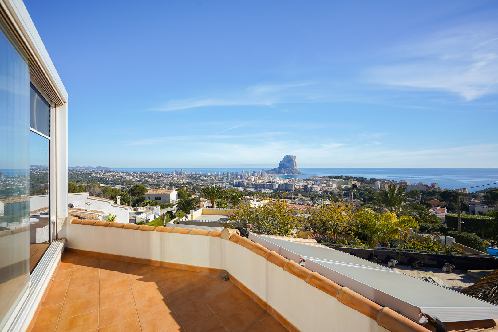 Terraza superior con suelo de gres cerámico y vistas despejadas al Peñón de Ifach, el skyline de Calpe y el mar. Se observa la instalación fotovoltaica en el nivel inferior.