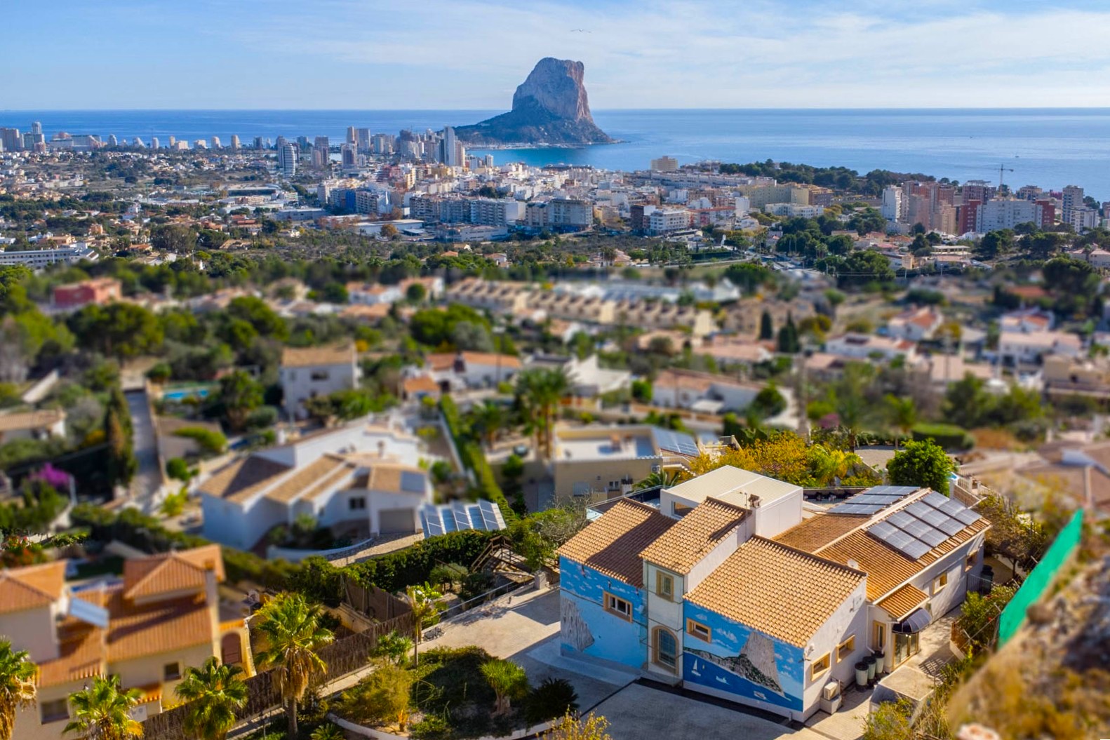 Vista aérea de la villa con paneles solares y mural decorativo, ofreciendo una panorámica del skyline de Calpe y el Peñón de Ifach sobre el Mediterráneo.