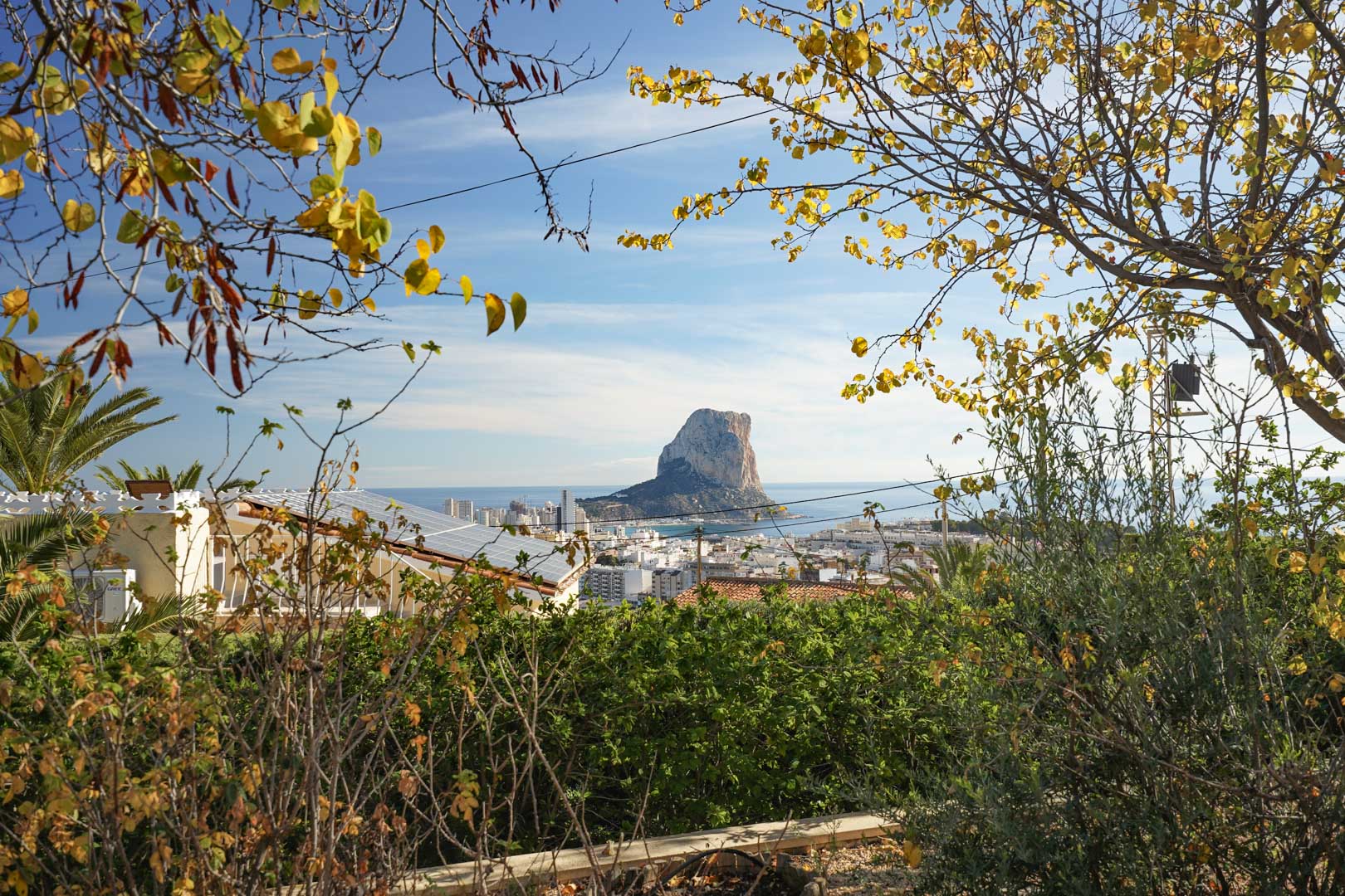 Vista panorámica del Peñón de Ifach y el skyline de Calpe desde la propiedad, destacando la instalación de paneles solares sobre la cubierta rodeada de vegetación mediterránea.