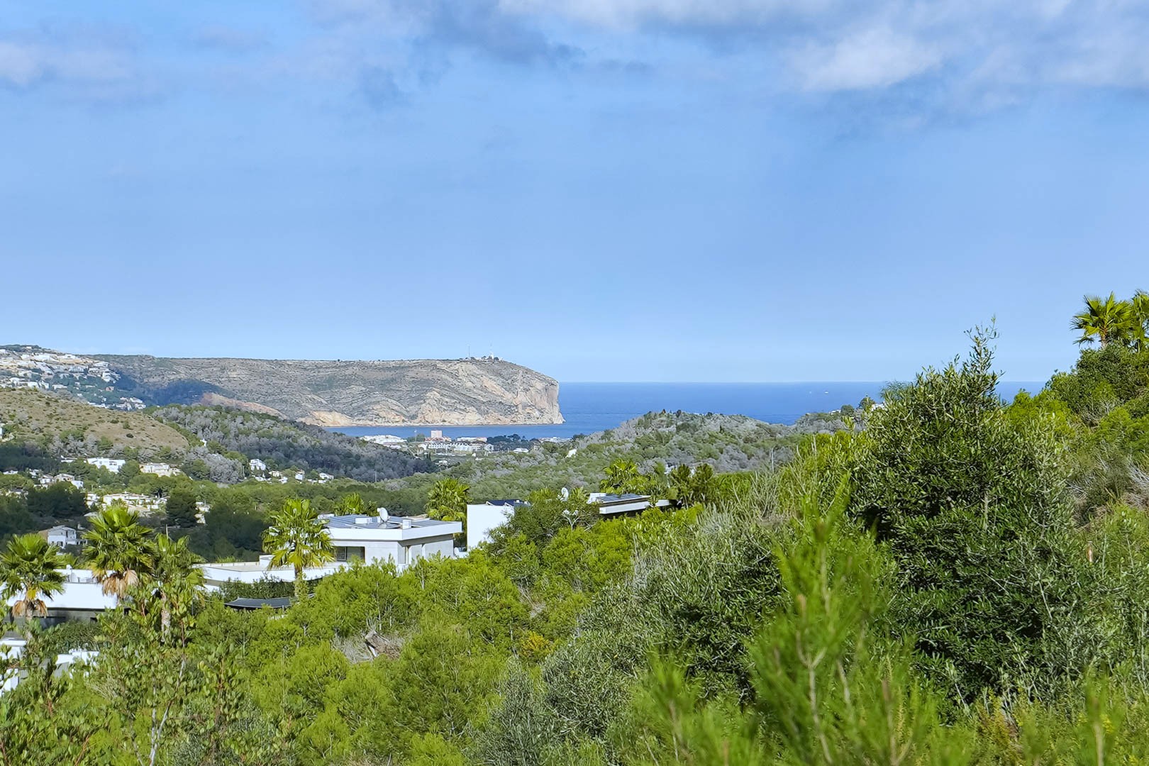 Vista panorámica desde la parcela hacia el mar Mediterráneo y el Cabo de San Antonio, rodeada de vegetación autóctona y villas de diseño moderno.