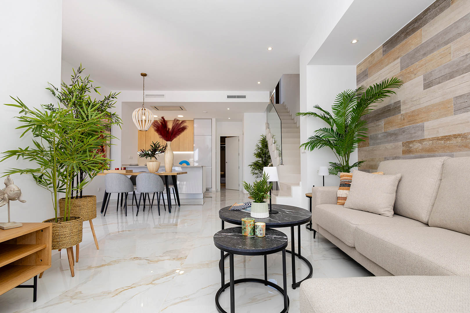 Salón-comedor de concepto abierto con suelos de porcelánico efecto mármol, pared de acento en madera y escalera con barandilla de cristal.
