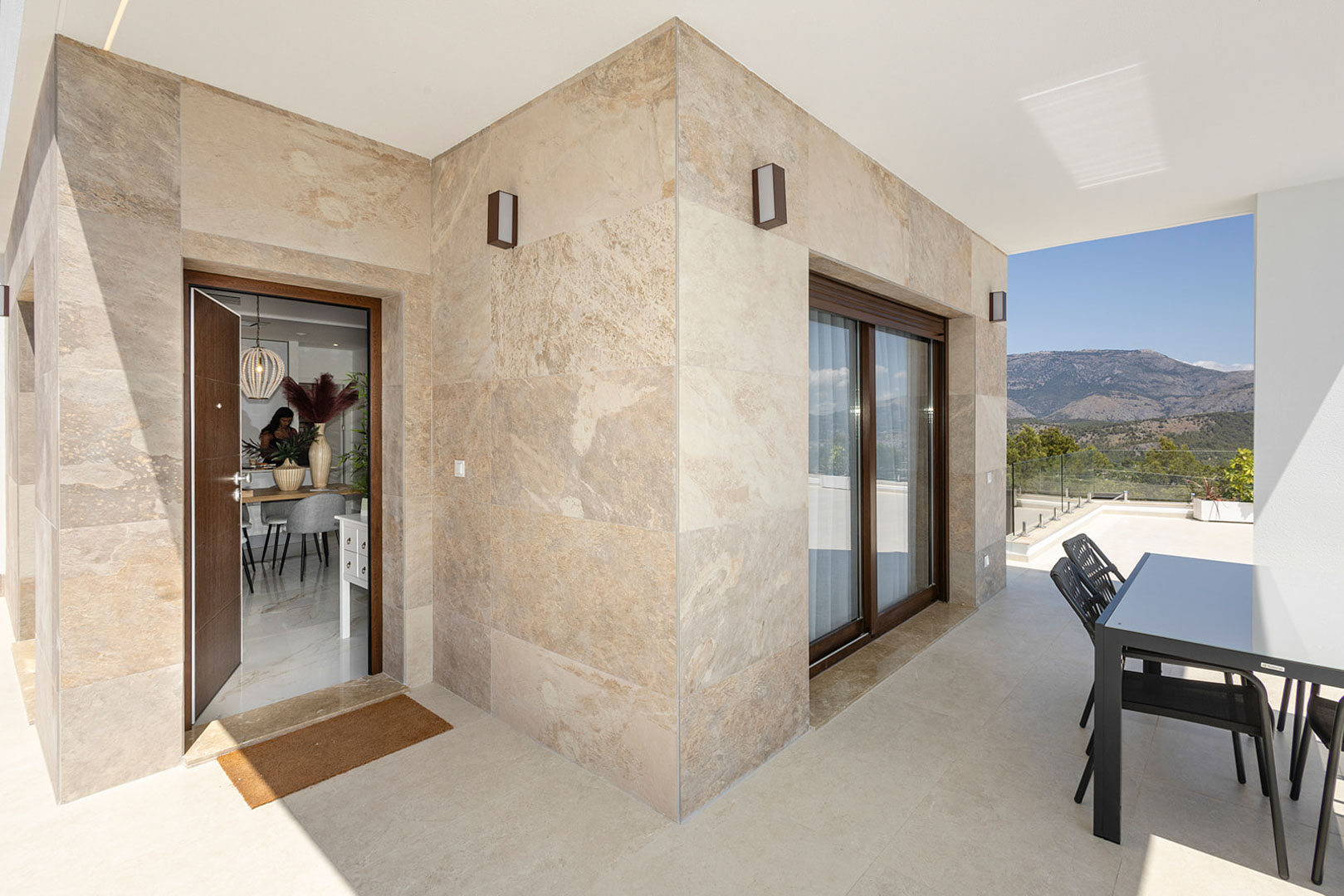 Terraza exterior con fachada de piedra natural, zona de comedor y vistas a la montaña. El acceso conecta directamente con el interior de la vivienda.