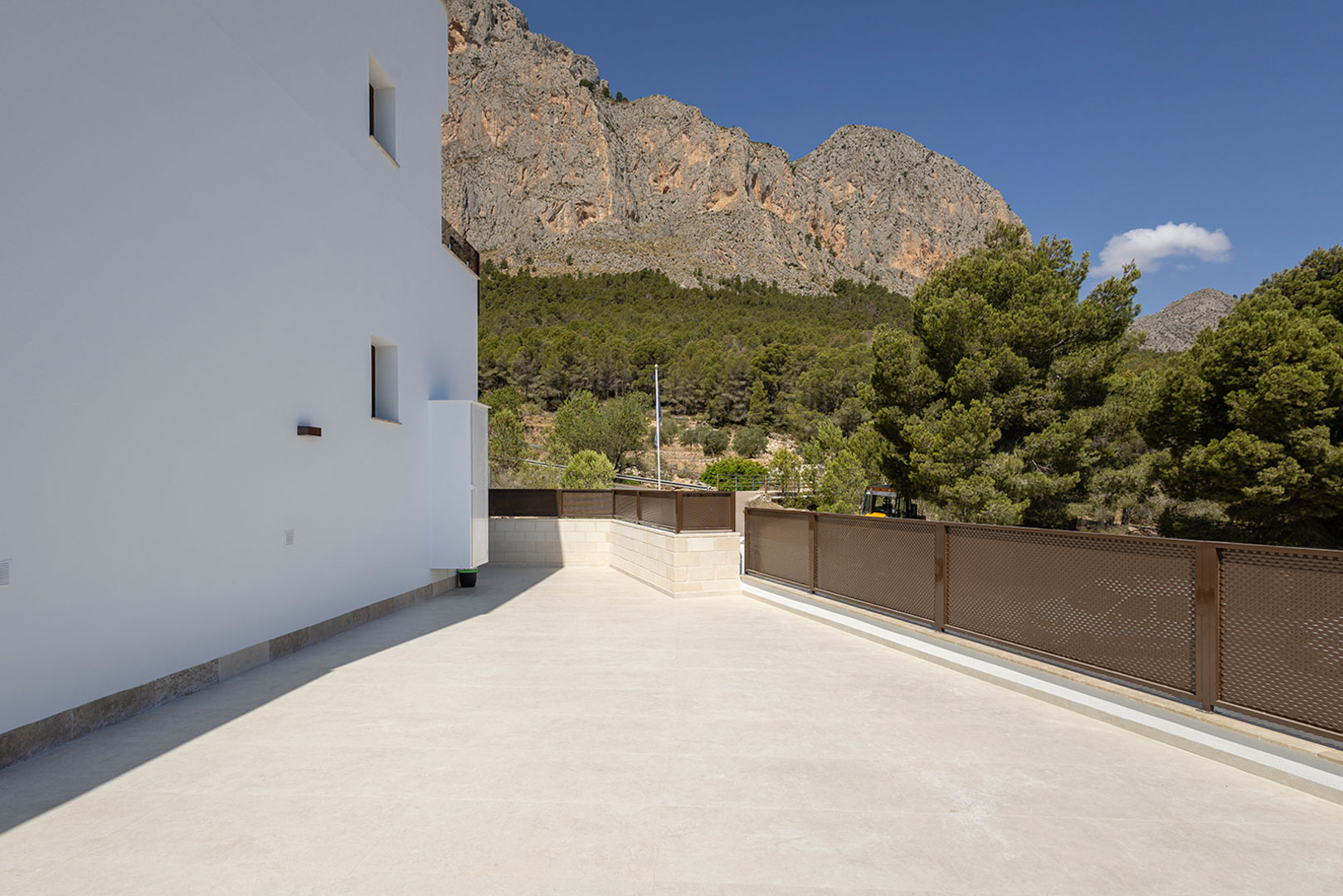Terraza exterior con pavimento de piedra clara y barandilla metálica calada, ofreciendo vistas despejadas a la montaña y al entorno forestal circundante.