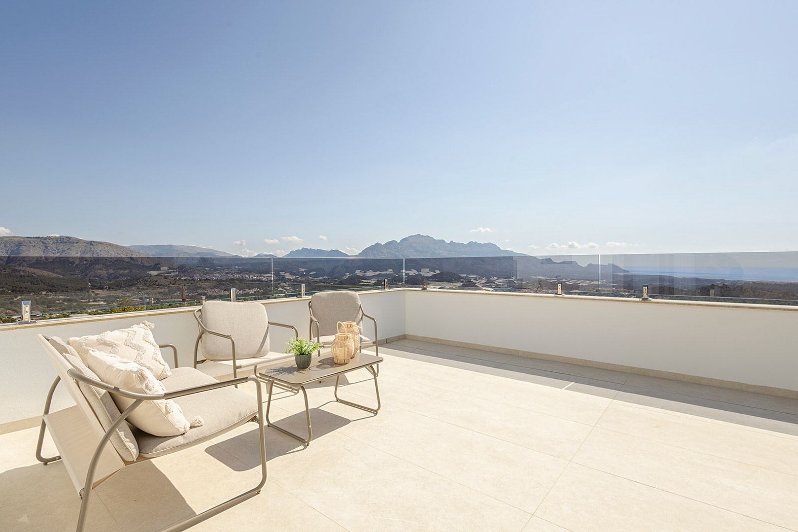 Terraza solárium con suelo de gres claro, barandilla de cristal de seguridad y mobiliario de exterior con vistas panorámicas al mar y la montaña.