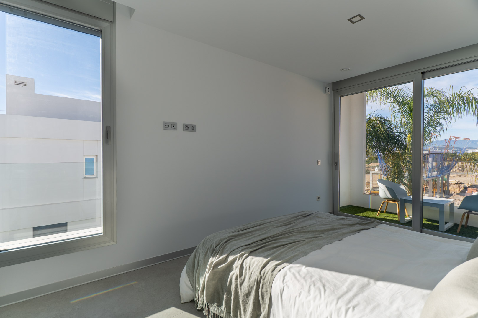 Dormitorio luminoso con acceso directo a una terraza privada con césped artificial. Destaca su diseño minimalista, suelos grises y carpintería de aluminio de alta calidad.