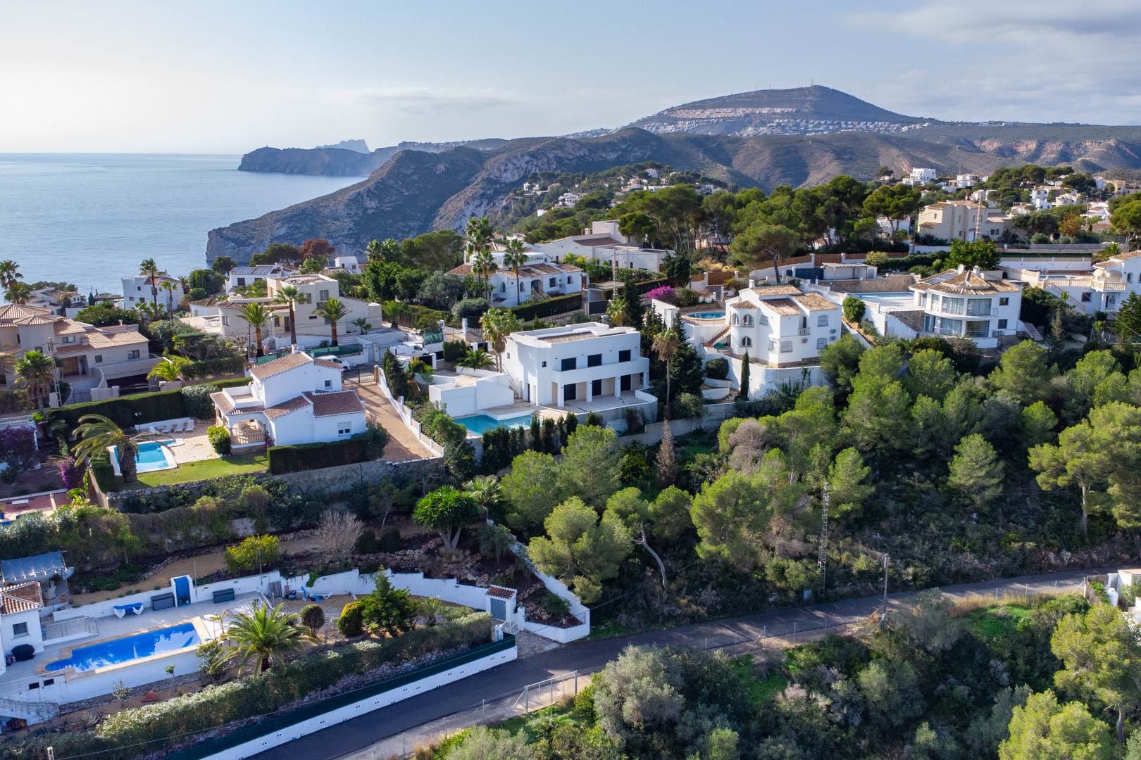 Vista aérea de la zona residencial en Granadella-Ambolo, mostrando villas integradas en la ladera con vistas al mar Mediterráneo y la costa escarpada.