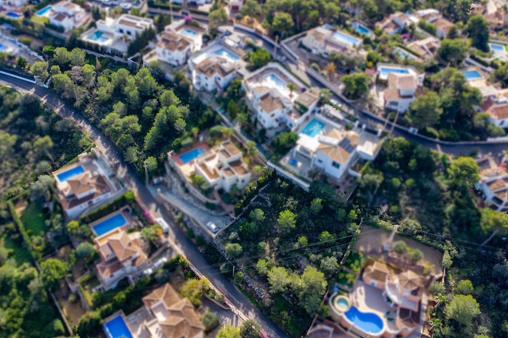 Vista aérea de la parcela edificable en Granadella-Ambolo, rodeada de villas con piscinas y abundante vegetación mediterránea en una zona residencial consolidada.