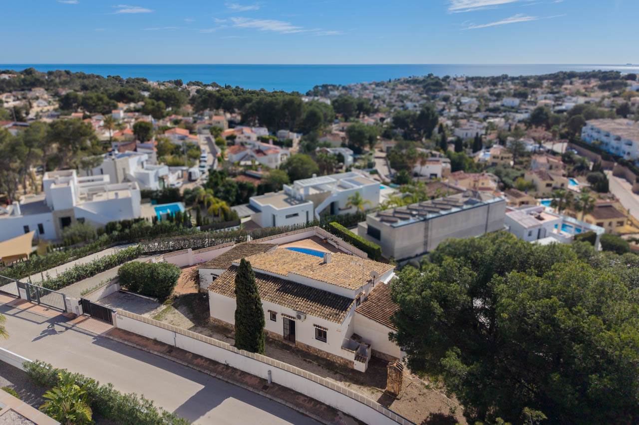Vista aérea de la villa en Benissa Costa, mostrando su arquitectura mediterránea con tejados de teja, parcela privada con ciprés y vistas despejadas al mar.