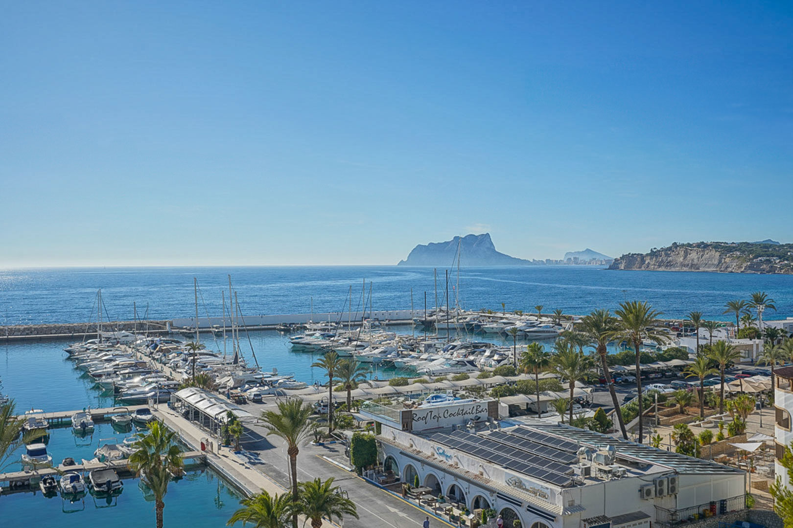 Vista panorámica del puerto deportivo de Moraira con el Peñón de Ifach al fondo, destacando los amarres, barcos de recreo y el entorno costero mediterráneo.