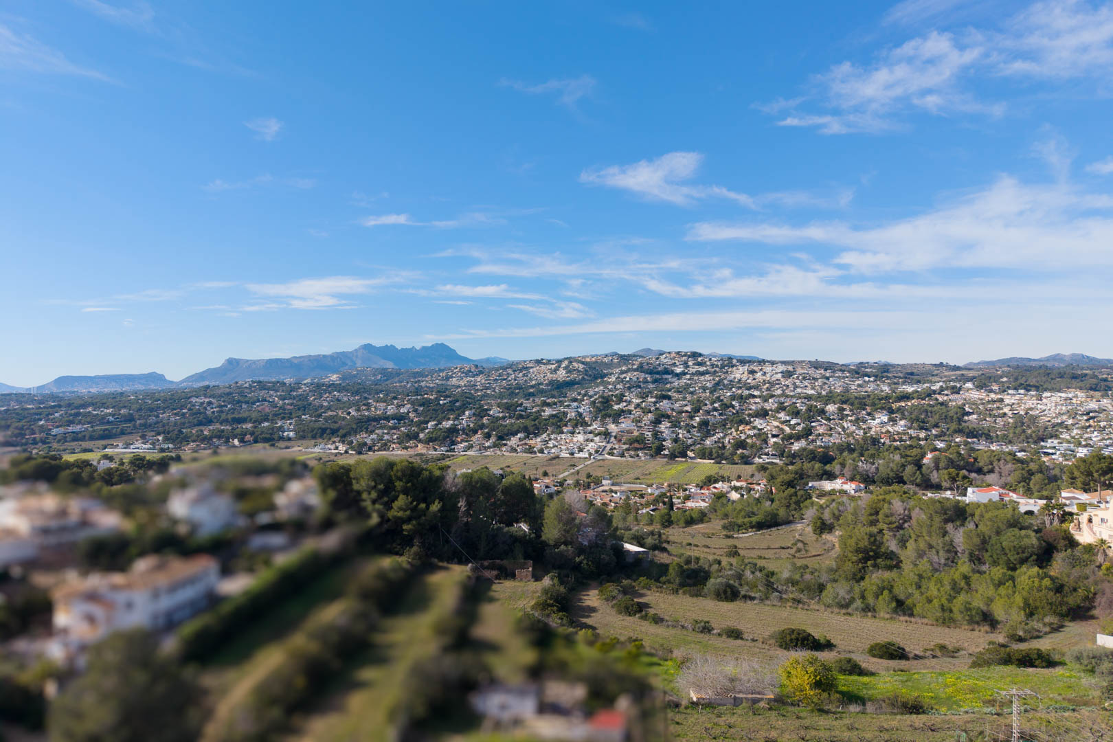Vista panorámica elevada del valle de Moraira, mostrando la integración de zonas residenciales con el paisaje mediterráneo y montañas al fondo.