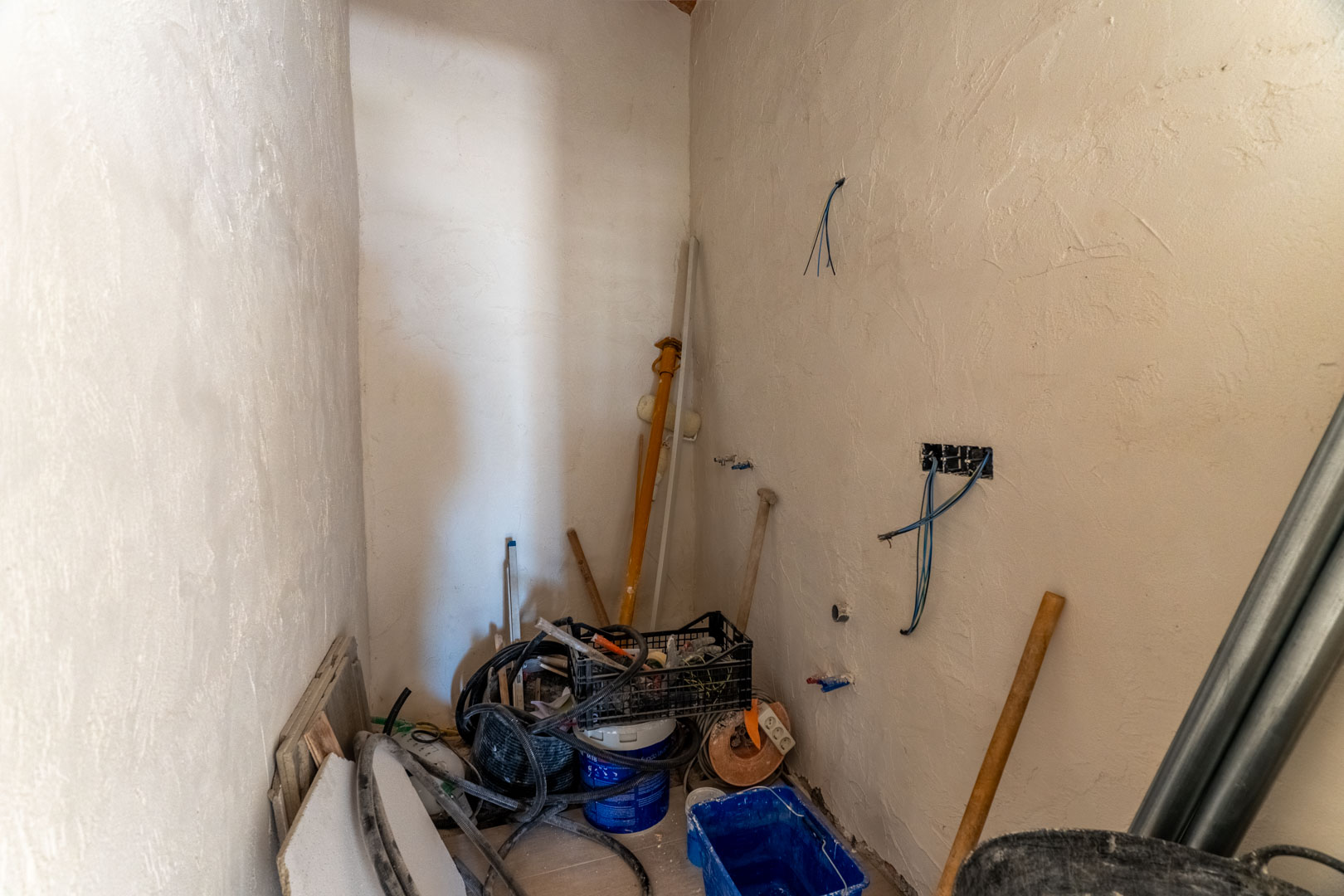 Espacio interior en proceso de reforma con paredes enfoscadas, instalaciones eléctricas visibles y materiales de construcción listos para su finalización.