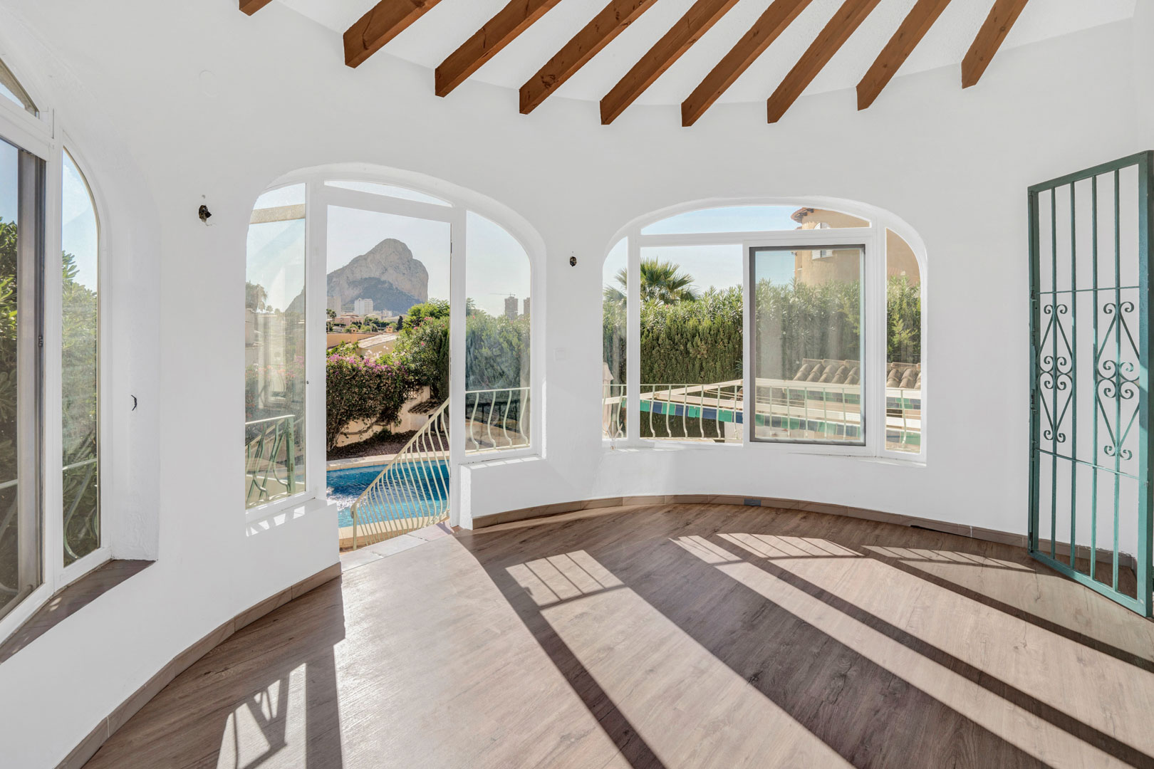 Terraza acristalada con vigas de madera vista, suelos laminados y ventanales en arco que ofrecen vistas directas al Peñón de Ifach y la piscina privada.