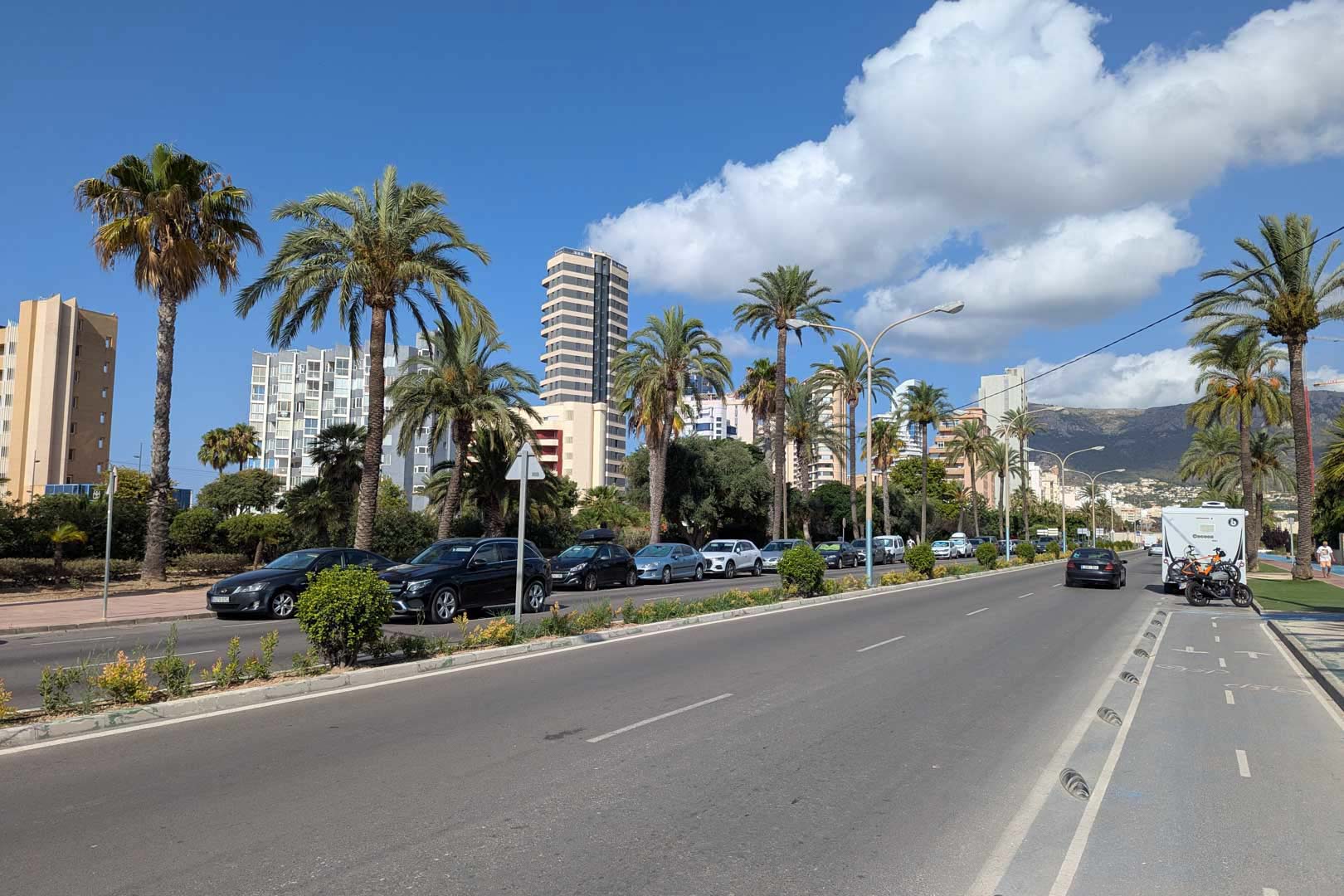 Vista de la avenida principal en Calpe con palmeras, carril bici y edificios residenciales, mostrando el entorno urbano y los servicios cercanos a la propiedad.