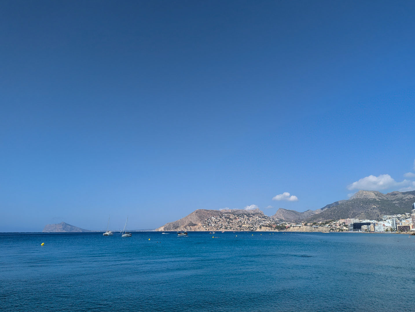 Vistas panorámicas del mar Mediterráneo y la costa de Calpe con embarcaciones de recreo y montañas en el horizonte bajo un cielo despejado.