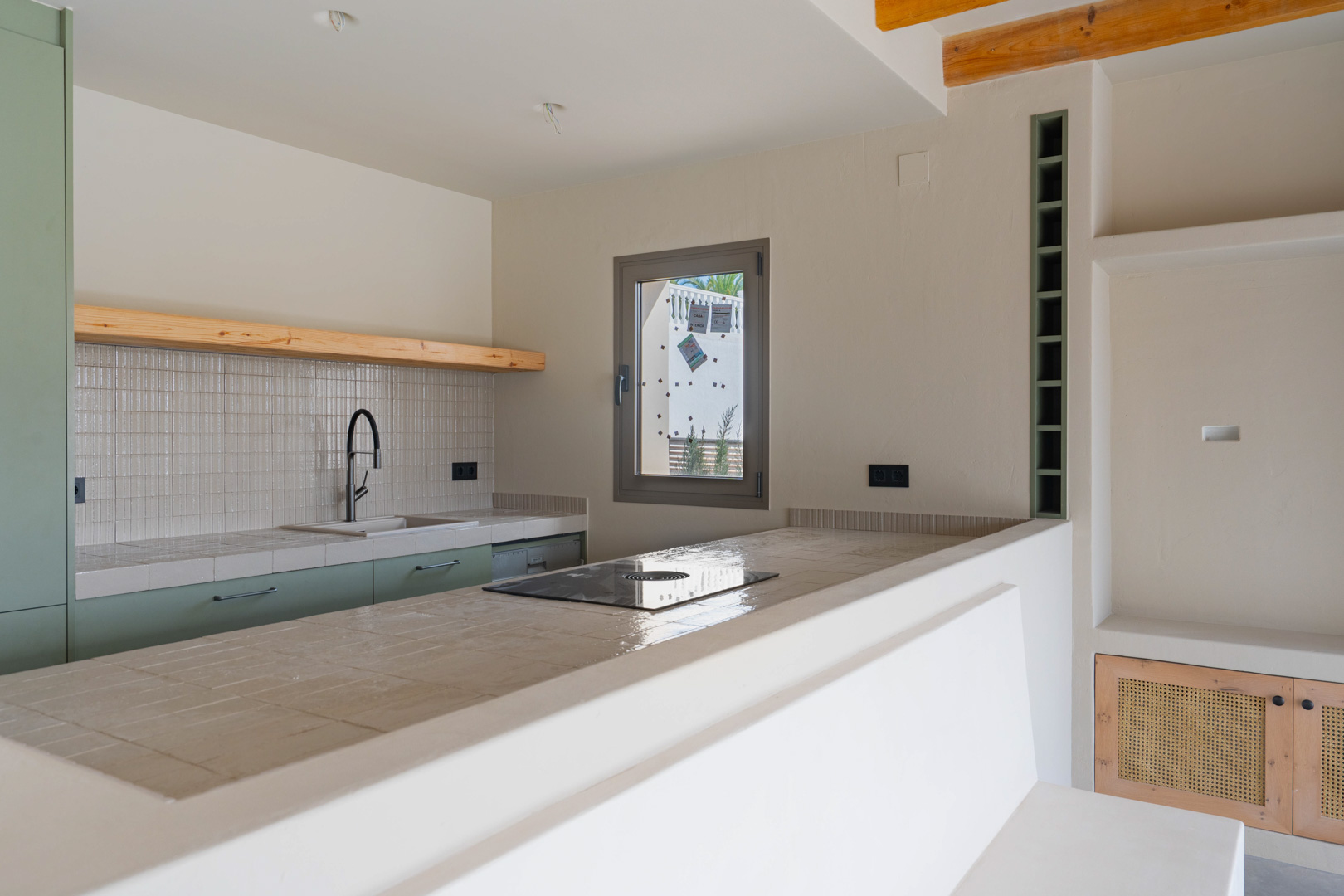 Cocina de diseño con encimeras de porcelana, placa de inducción integrada y mobiliario verde salvia. Incluye acabados de arcilla artesanal y estanterías de madera natural.