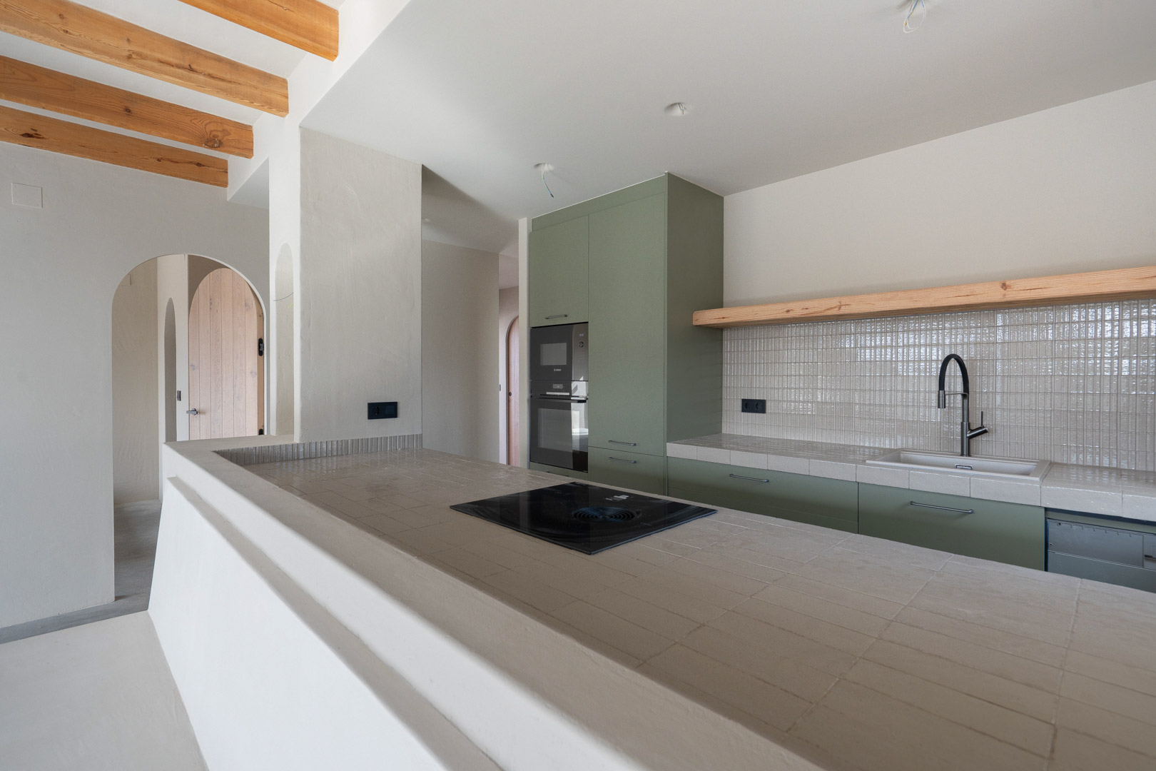 Cocina de diseño con muebles verde salvia, encimeras de porcelana Ragno y placa Bora. Incluye vigas de madera vista y acabados en arcilla de Matteo Brioni.
