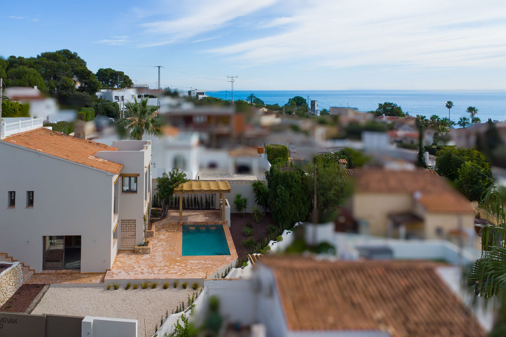 Vista elevada de la villa con piscina privada, terraza de terracota y pérgola de madera, ofreciendo vistas despejadas al mar Mediterráneo y al entorno residencial.