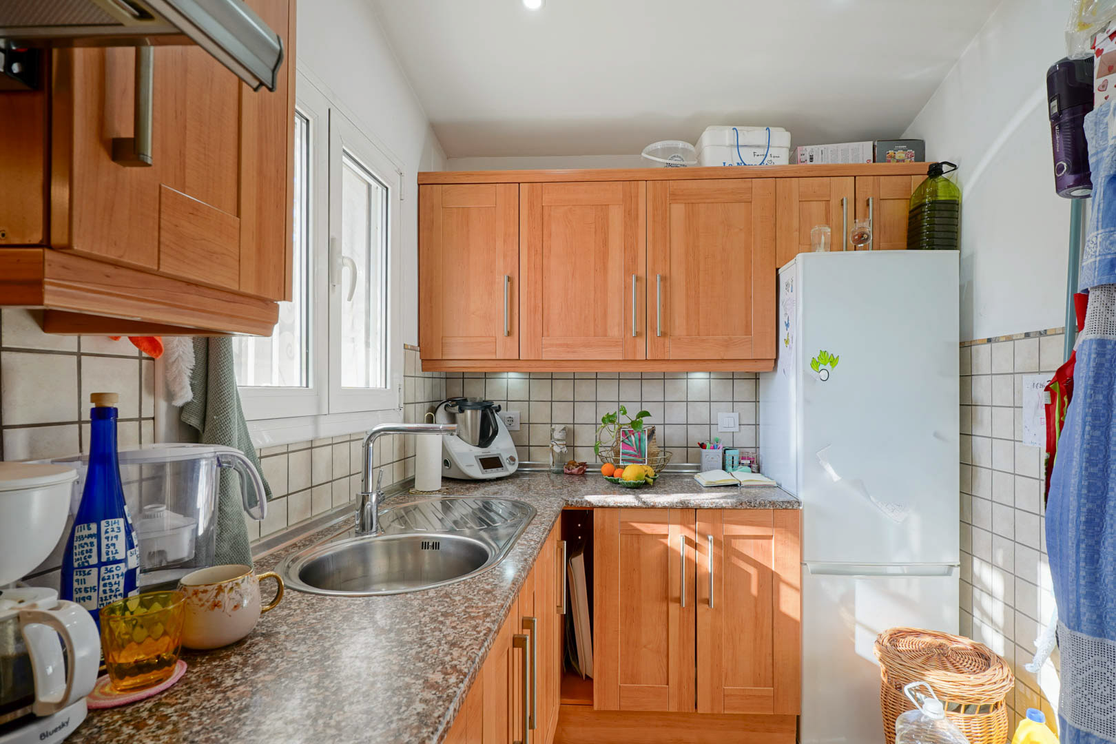 Cocina independiente con mobiliario de madera, encimera de granito y fregadero de acero inoxidable. Dispone de luz natural a través de una ventana lateral y armarios superiores.
