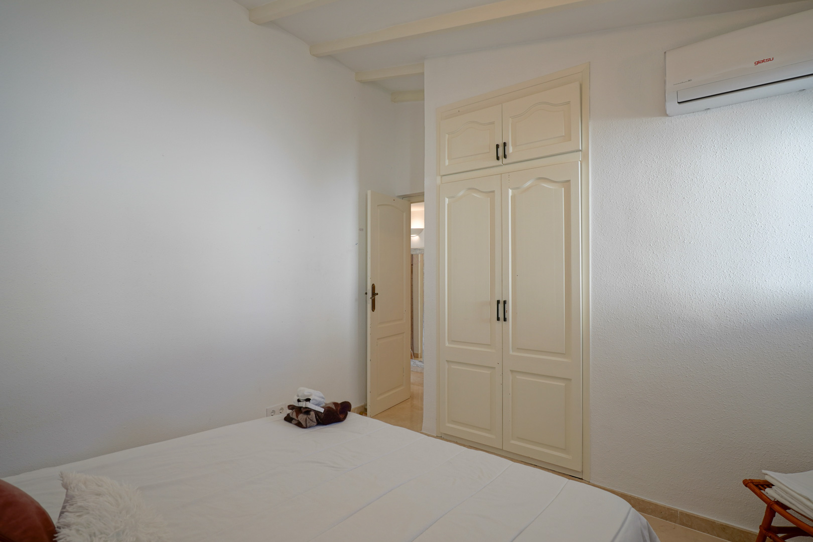 Dormitorio luminoso con armario empotrado de puertas clásicas, vigas de madera vistas en el techo y sistema de aire acondicionado tipo split.
