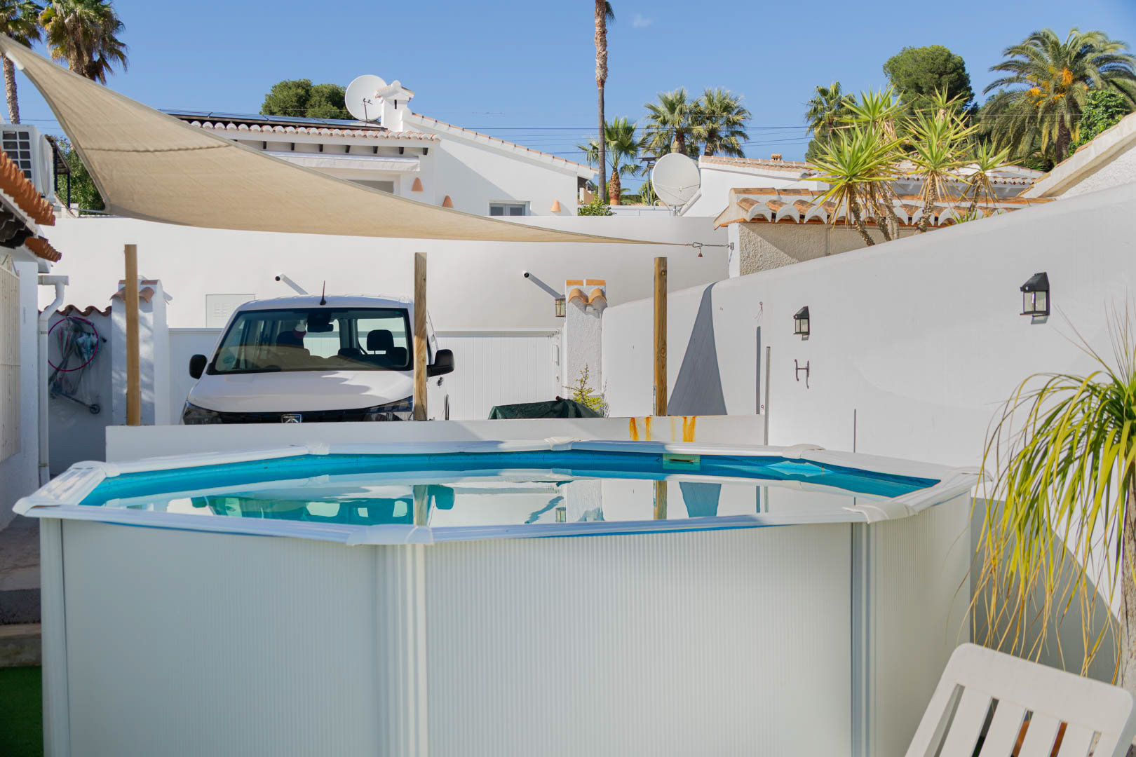 Piscina portátil de diseño octogonal situada en una terraza soleada con toldo de vela, rodeada de muros blancos y vegetación mediterránea.