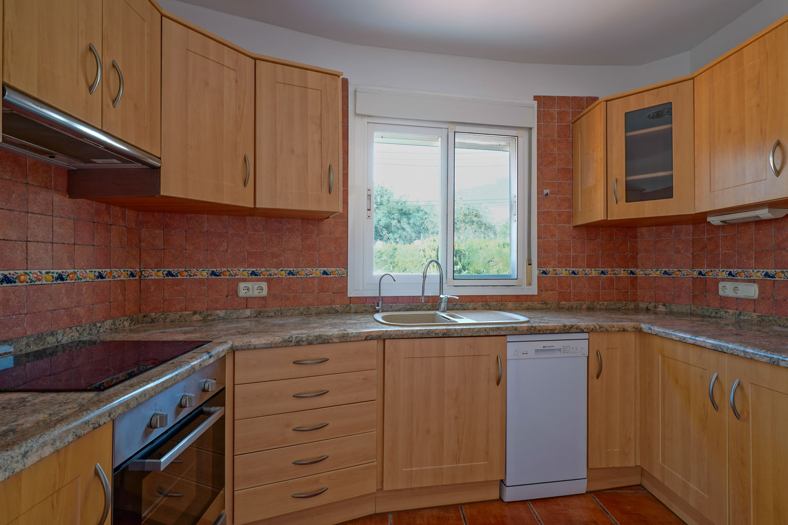 Cocina independiente equipada con armarios de madera, encimera de granito y salpicadero de azulejos rústicos. Incluye electrodomésticos integrados y ventana con luz natural.