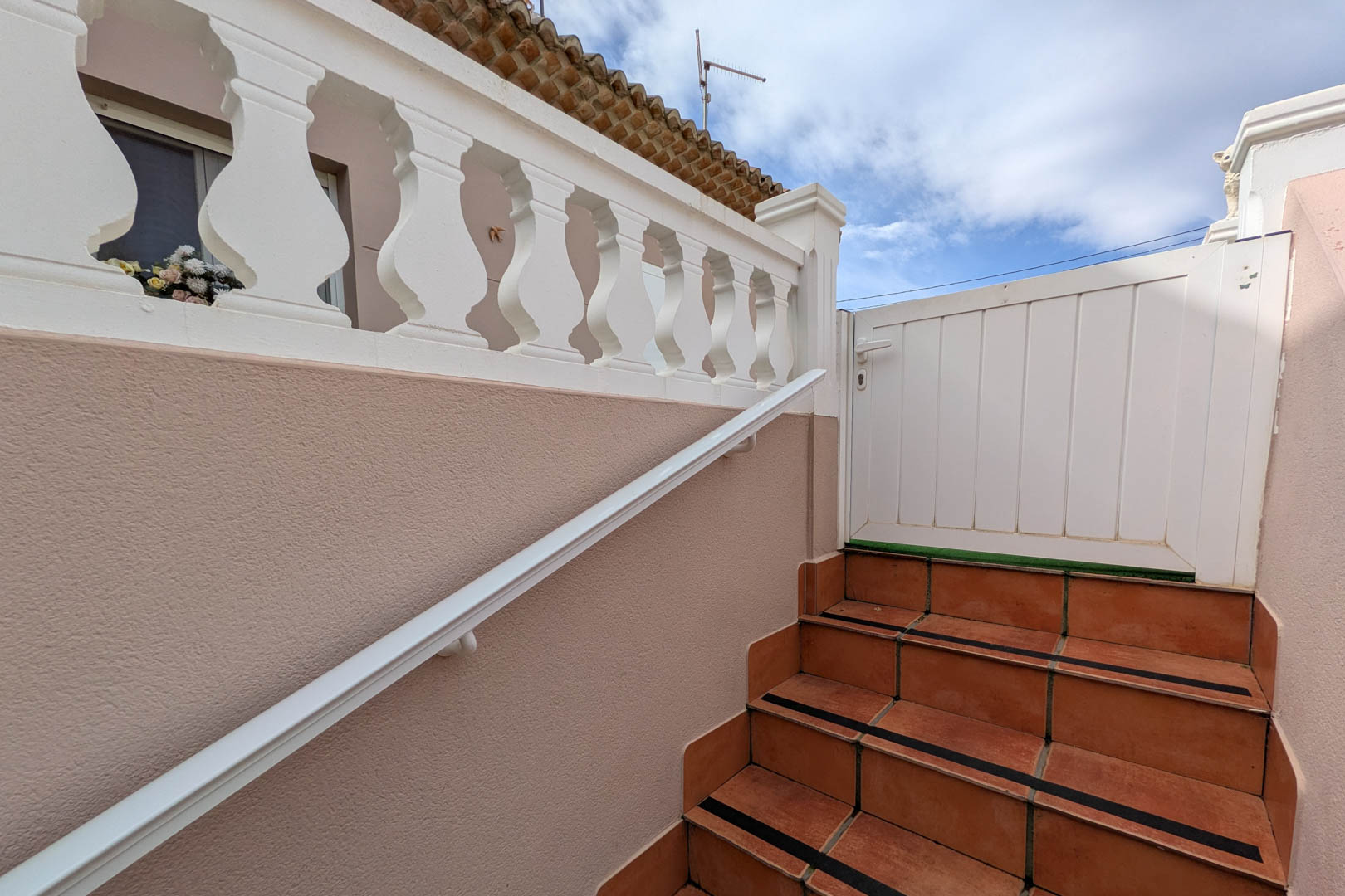 Escalera exterior de acceso con peldaños de gres, bandas antideslizantes, pasamanos blanco y balaustrada clásica que conduce al portón de entrada de la planta superior.