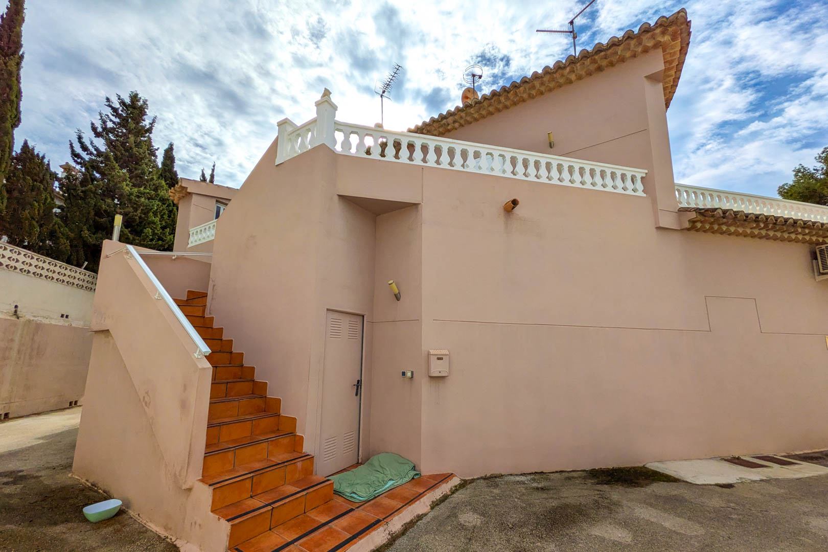 Escalera exterior de gres cerámico que conduce a la planta superior, con fachada en tonos salmón y terraza protegida por una balaustrada blanca tradicional.