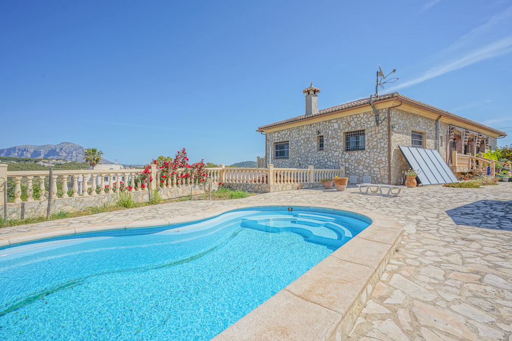 Exterior con piscina de forma curva y villa revestida de piedra natural. La terraza pavimentada ofrece vistas despejadas a las montañas y balaustradas clásicas.