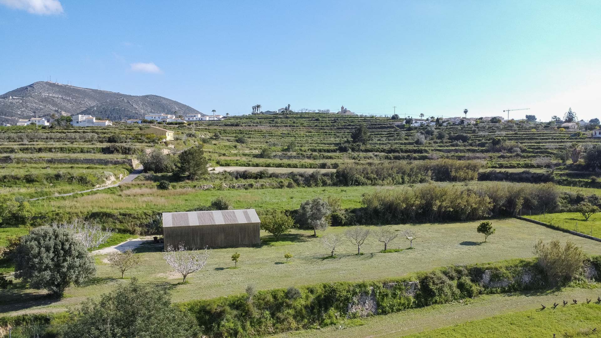 Vista aérea de laderas abancaladas con muros de piedra tradicionales, incluyendo un cobertizo de madera y árboles frutales en un entorno rural.