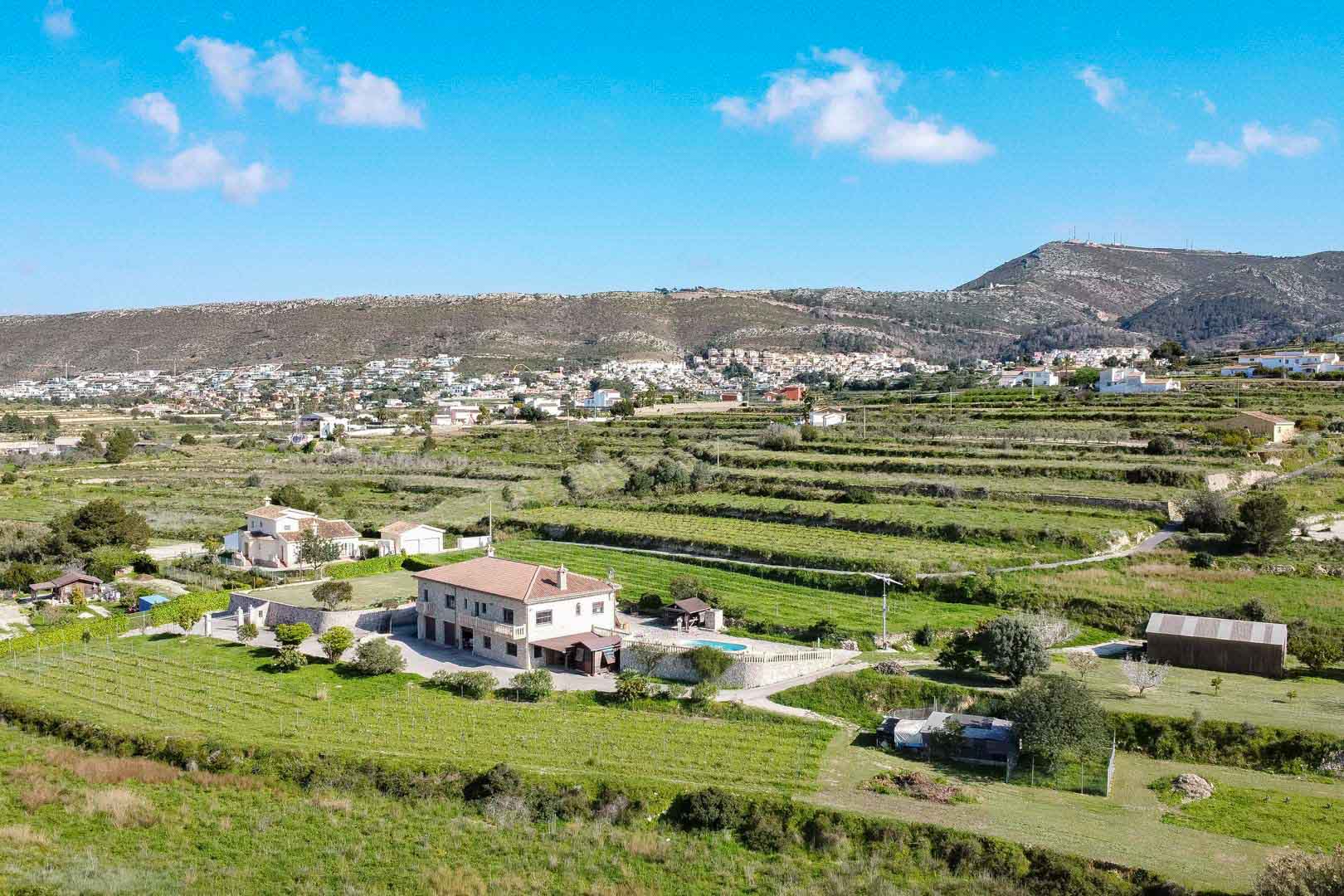 Vista aérea de una residencia de piedra de dos plantas con piscina y terrenos agrícolas aterrazados con vistas a las montañas.