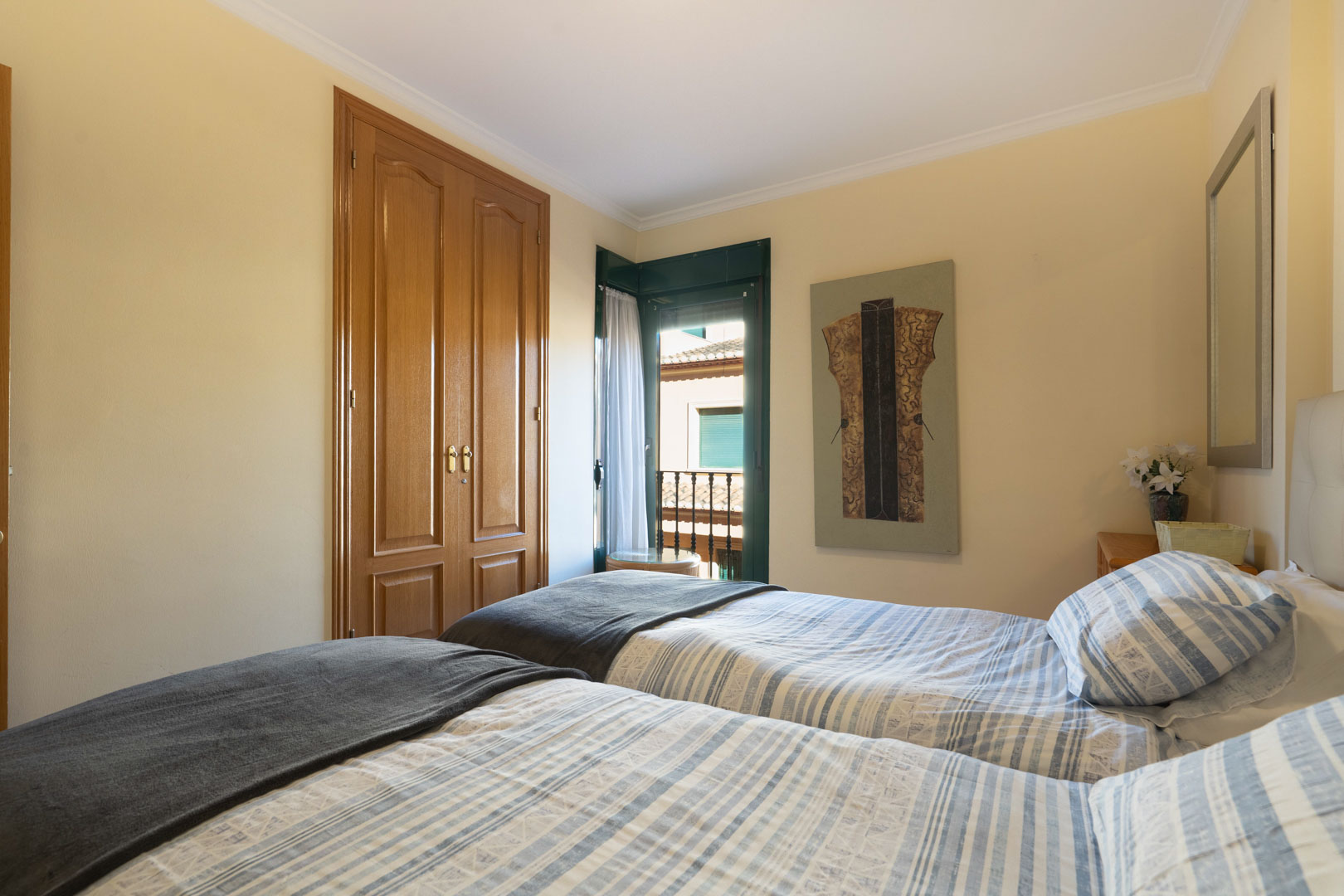 Dormitorio luminoso con dos camas individuales, armario empotrado de madera y acceso directo a un balcón con persianas tradicionales.