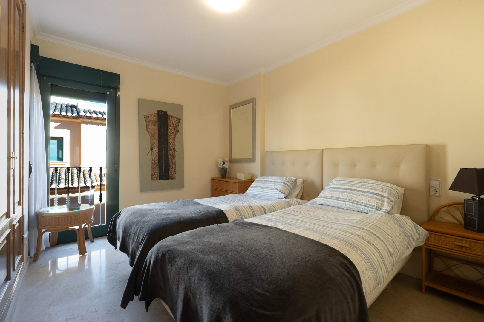 Dormitorio luminoso con dos camas individuales, cabecero acolchado, suelos de mármol y armarios empotrados. Incluye acceso directo a un balcón privado.