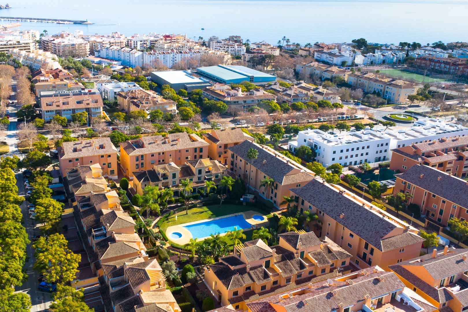 Vista aérea del complejo Floridamar en Jávea, mostrando la piscina comunitaria rodeada de jardines y la cercanía al puerto y al mar Mediterráneo.