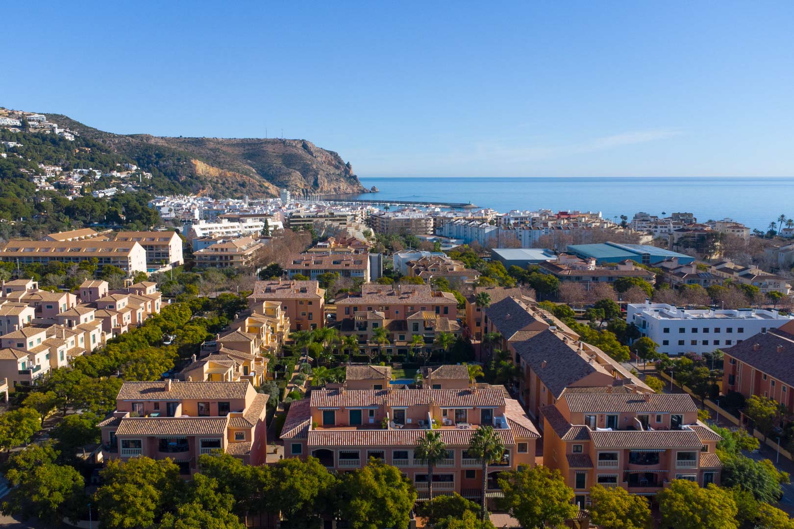 Vista aérea del complejo Floridamar en Jávea, mostrando su arquitectura mediterránea rodeada de vegetación con el puerto y el Cabo de San Antonio al fondo.