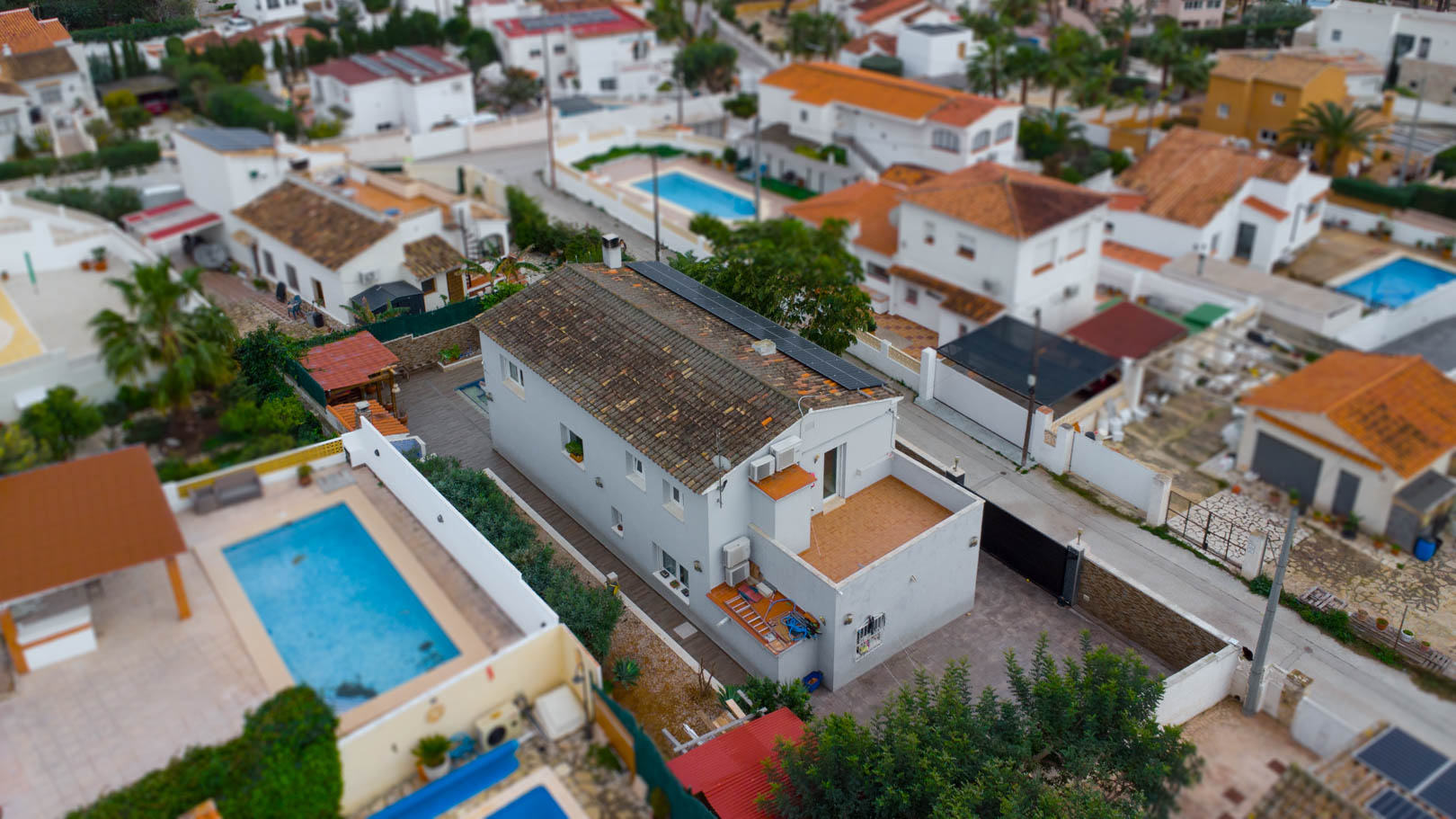 Vista aérea de la villa que destaca el tejado inclinado con paneles solares fotovoltaicos, la terraza superior y el entorno residencial consolidado de Calpe.