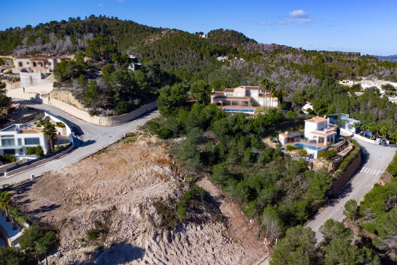 Parcela elevada en esquina dentro de la urbanización Tosalet 5, rodeada de pinos y villas modernas, con acceso por viales asfaltados y vistas al entorno natural.