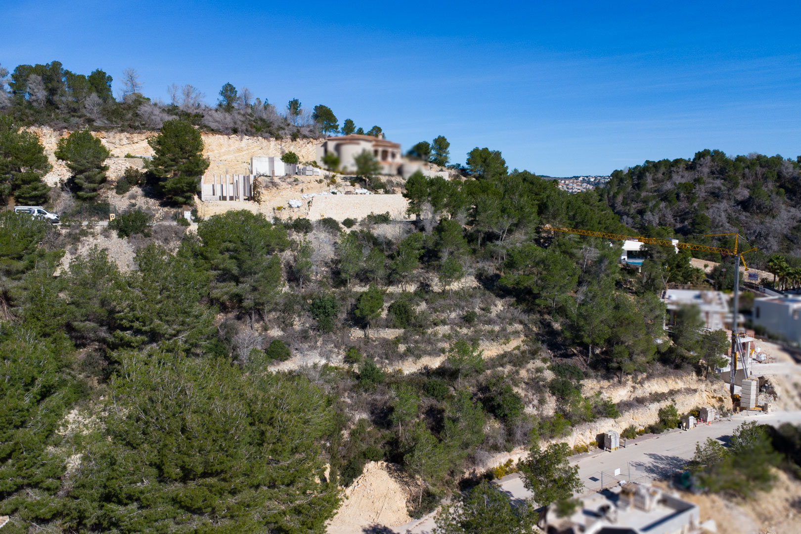 Vista aérea de una parcela en pendiente con pinos mediterráneos, muros de contención de piedra y obras en curso en la urbanización Tosalet 5.