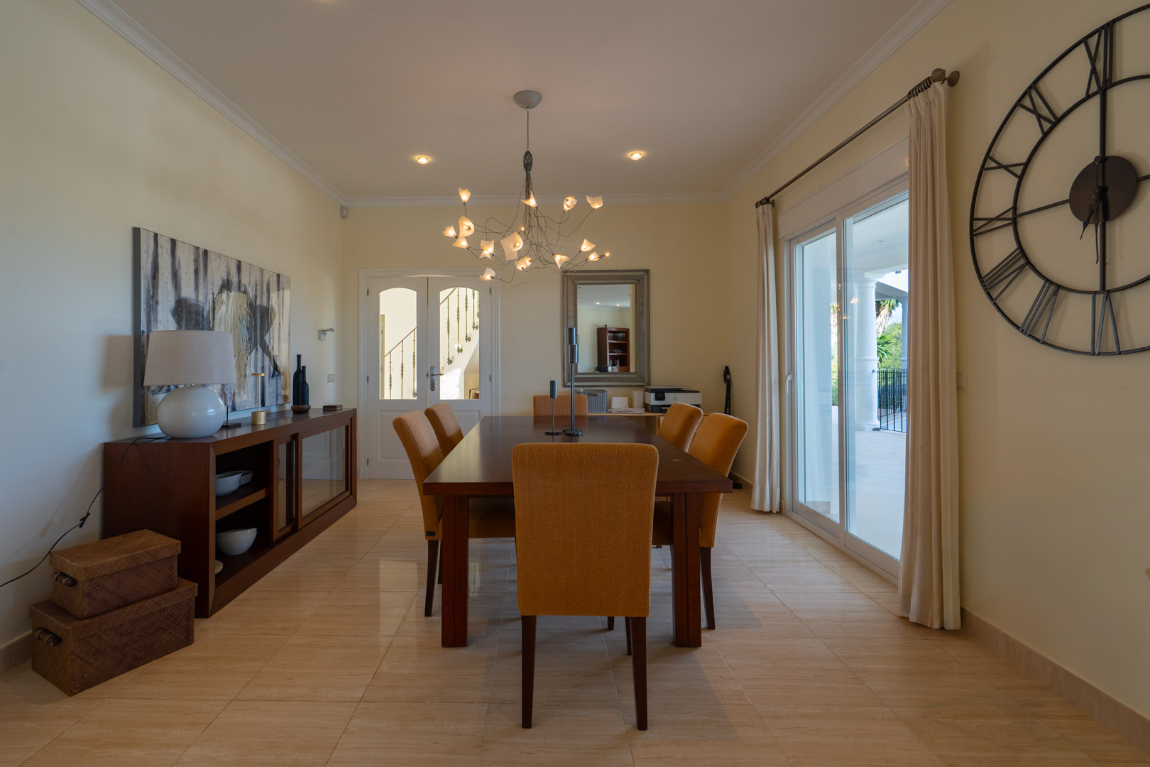 Comedor elegante con mesa de madera noble, sillas tapizadas en tono mostaza y acceso directo a la terraza mediante amplios ventanales correderos.