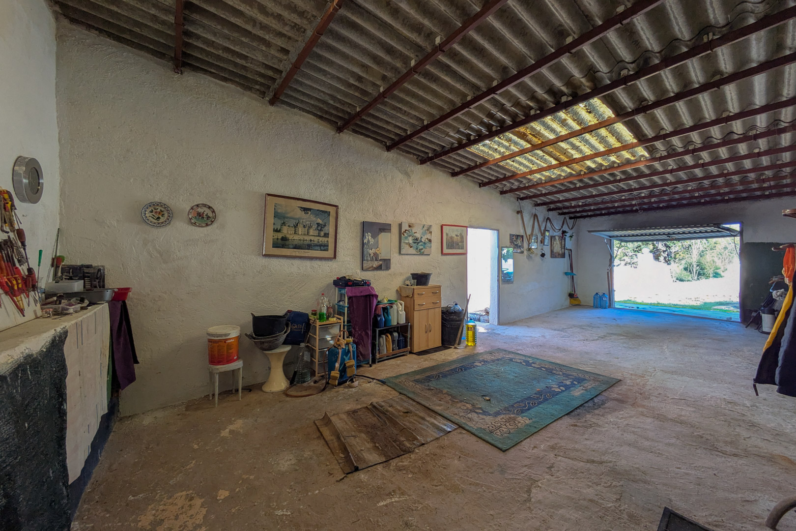 Amplio espacio de garaje o taller con suelos de hormigón, paredes encaladas y techos altos con tragaluz que aporta luz natural directa.
