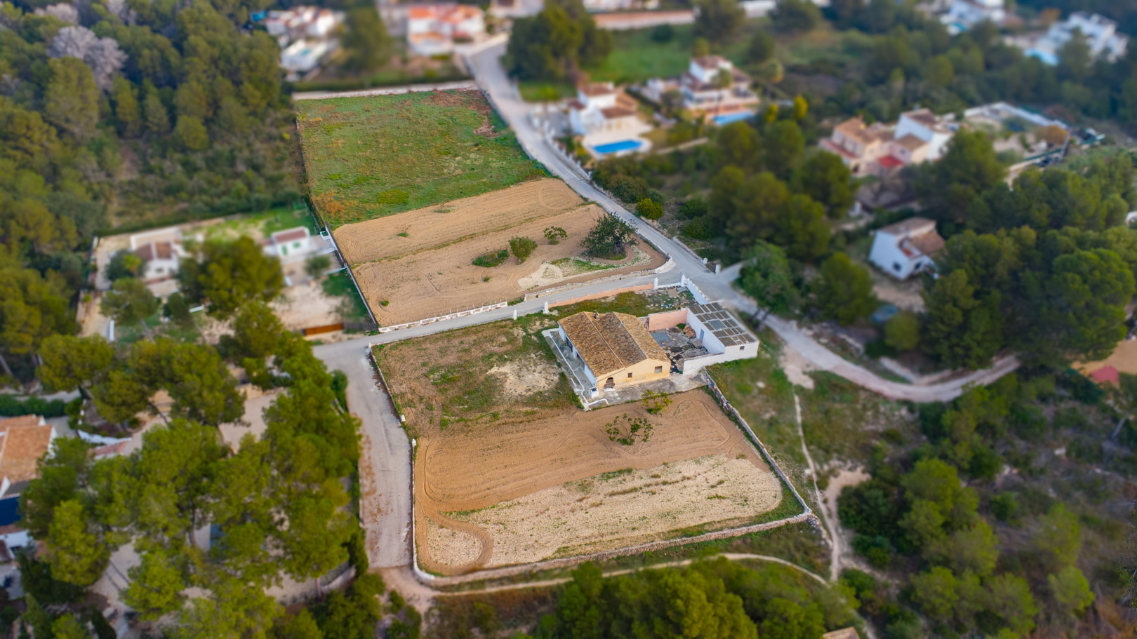 Vista aérea que muestra la finca tradicional y la extensión de las parcelas rústicas llanas, rodeadas de vegetación mediterránea y pinos en Jávea.