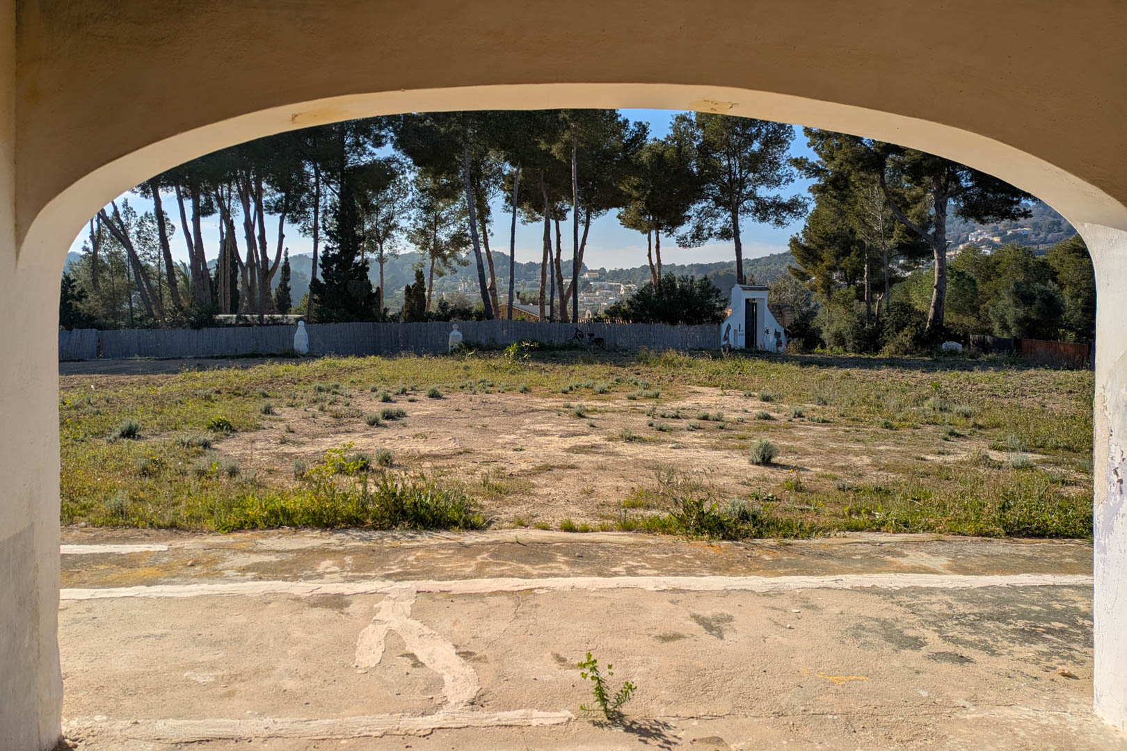 Vista desde el arco de la naya hacia la amplia parcela rústica, rodeada de pinos y vegetación mediterránea en un entorno tranquilo.