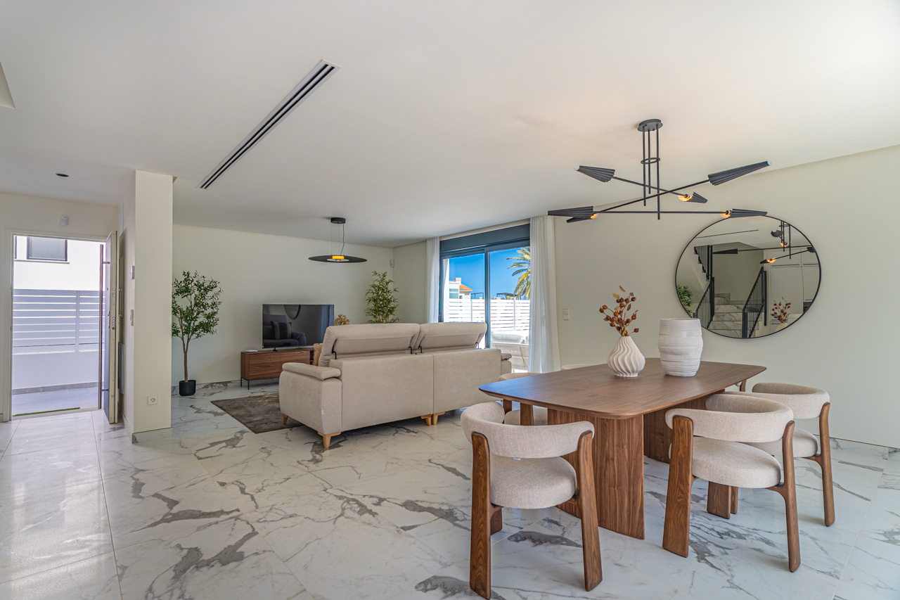 Salón-comedor diáfano con suelo de porcelánico efecto mármol, mesa de comedor de madera y acceso directo a la terraza a través de amplios ventanales.