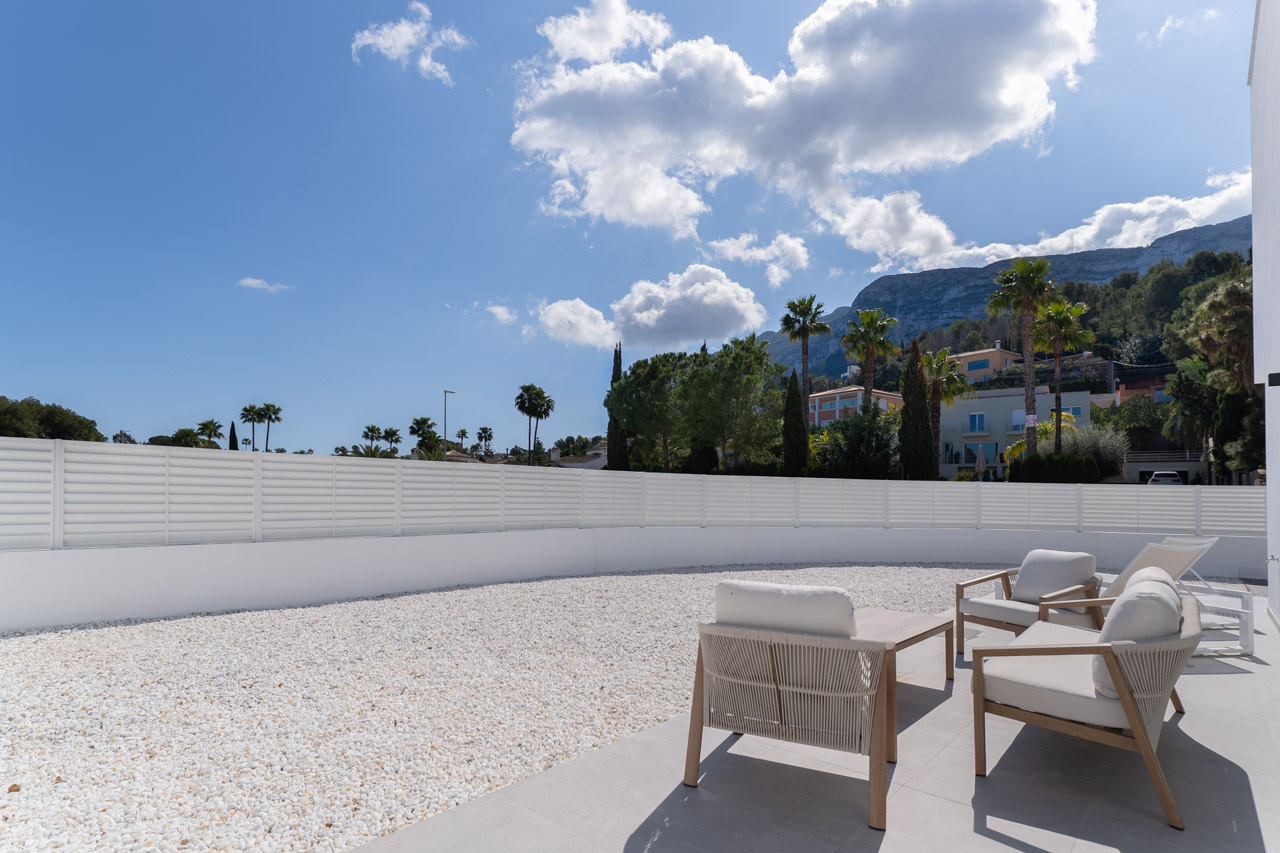 Terraza exterior con mobiliario de diseño, jardín de grava blanca perimetral y vistas directas al Parque Natural del Montgó en Dénia.