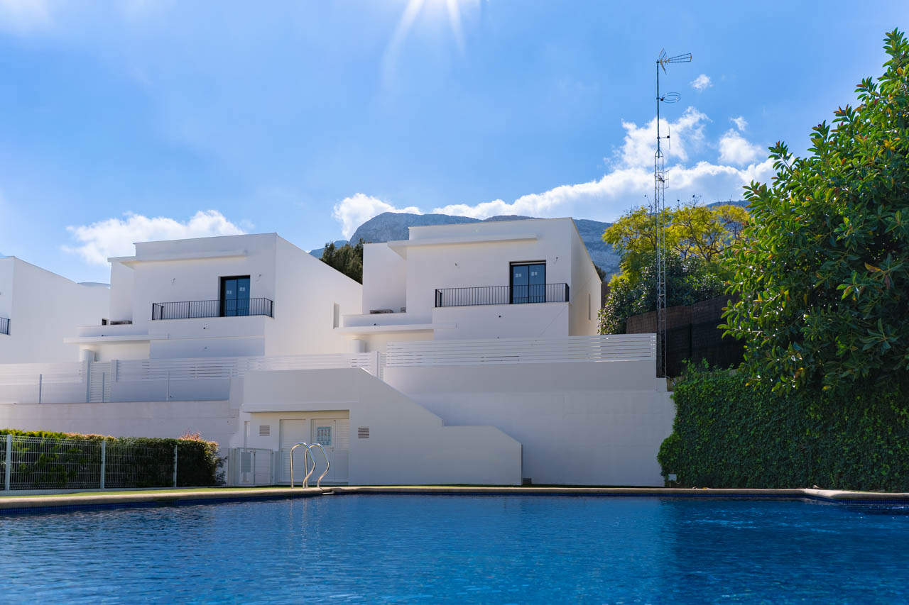 Vista de las villas modernas desde la piscina comunitaria, con fachadas blancas de diseño lineal y el macizo del Montgó como telón de fondo natural.